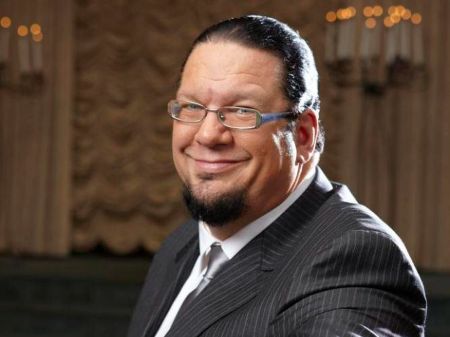 Penn Jillette in a black suit smiles at the camera.
